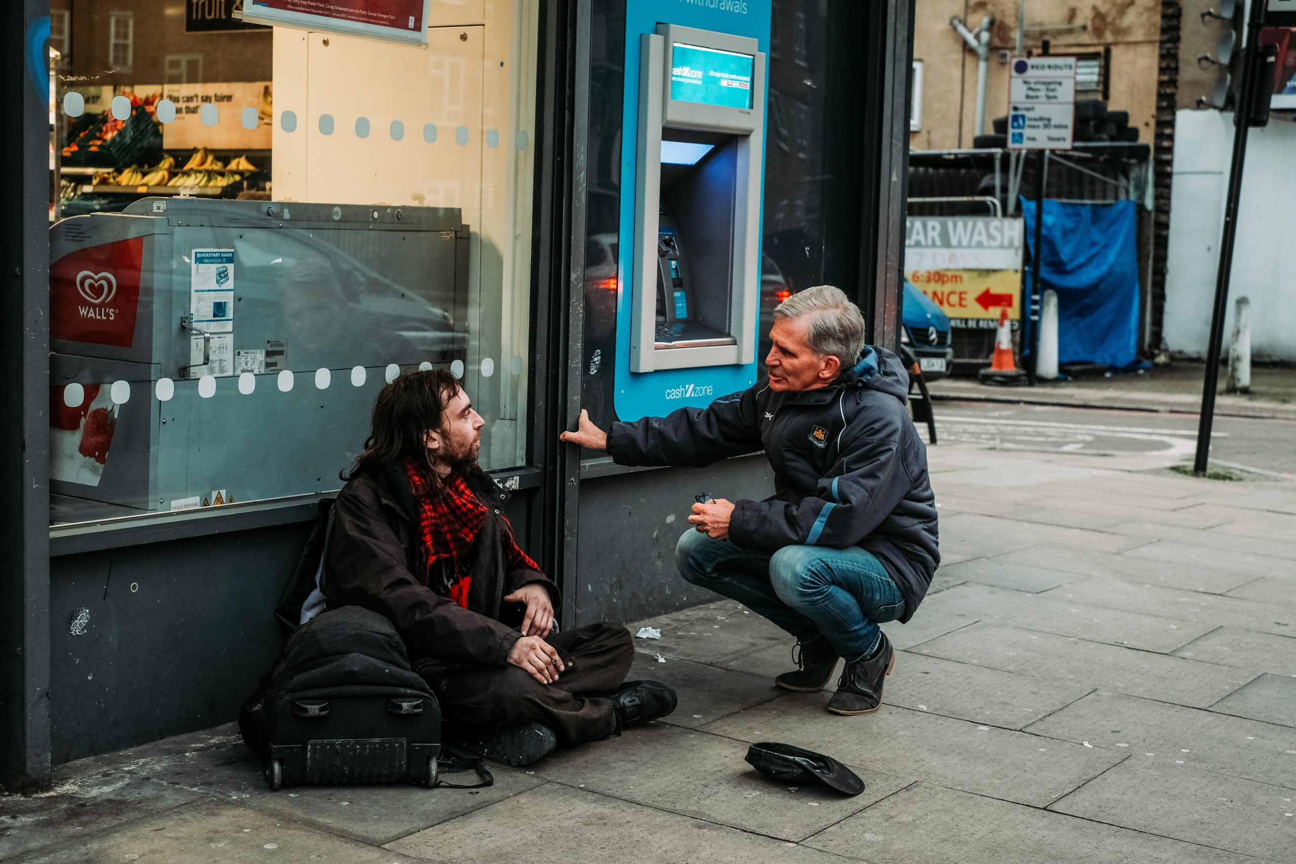 Stephen talking to a homeless man sitting on a street next to a cash point