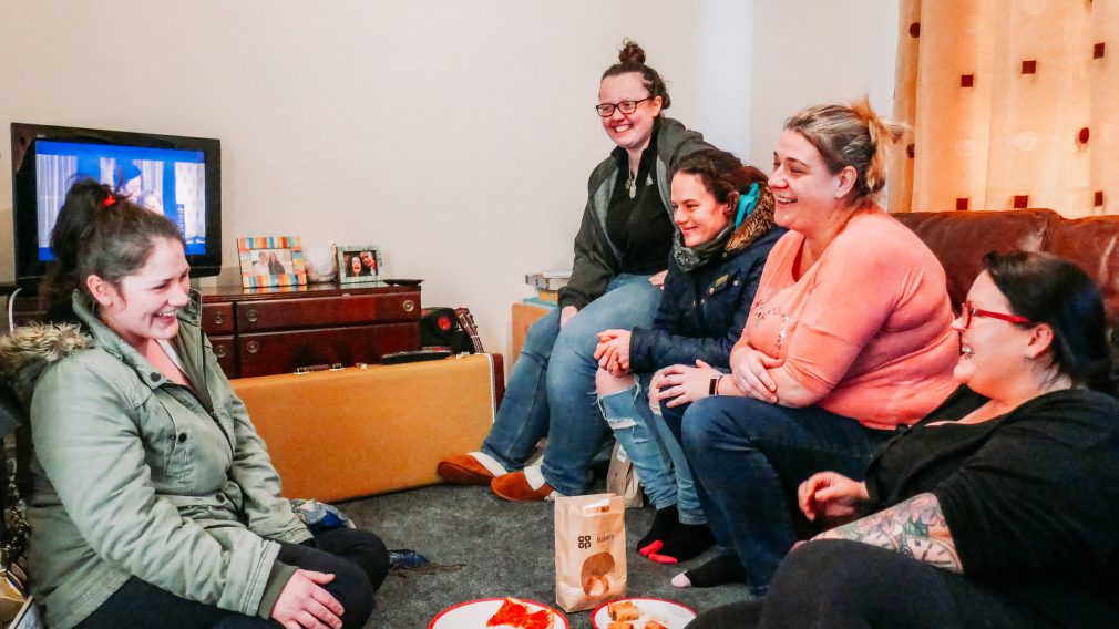 Amy and other women in a living room laughing and eating biscuits