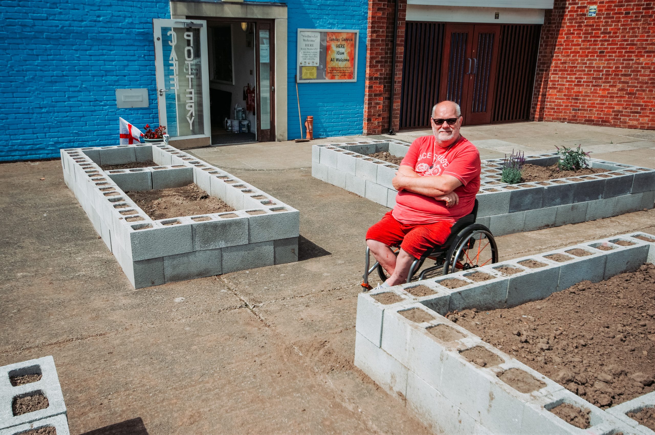 Sean is sat in his wheelchair surrounded by raised garden beds made of breezeblocks