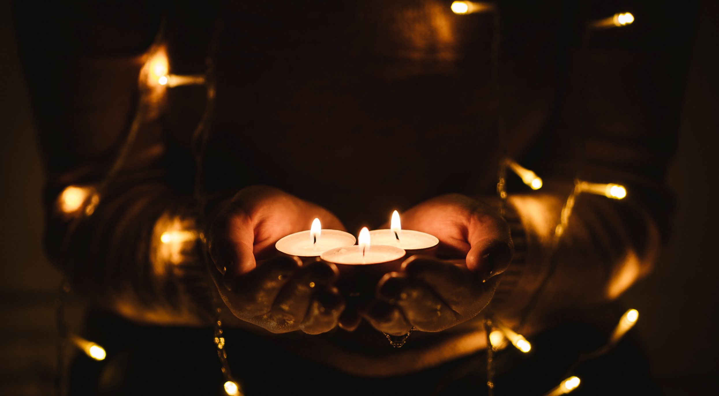 Person holding 3 candles and fairy lights